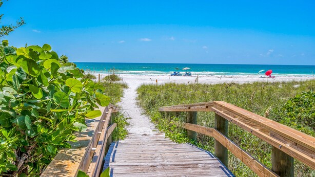 A wooden boardwalk leading to a beach with clear blue water and a few beach umbrellas. - Luxury home near the beach and shopping! Private backyard and pool! (Anna Maria)