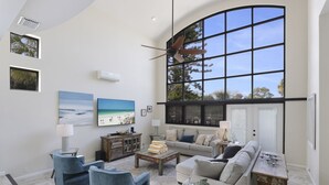 A spacious living room with a large window, a ceiling fan, and a television on the wall. - Luxury home near the beach and shopping! Private backyard and pool! (Anna Maria)