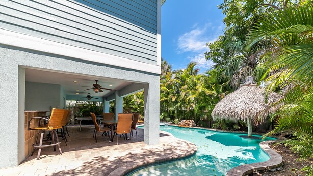 A pool area with a curved edge, outdoor seating, and a thatched-roof structure.