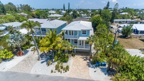 A two-story house with a balcony, surrounded by palm trees and a paved driveway.