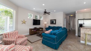 A spacious living room with a large sectional sofa, striped armchairs, and a flat-screen TV.