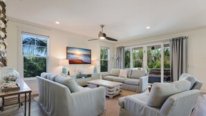 A spacious living room with a large TV, comfortable seating, and a view of palm trees.