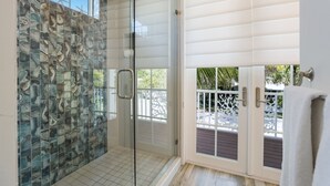 A glass-enclosed shower with a decorative tile backsplash, a sliding glass door leading to an outdoor area with a white railing, and a towel rack on the right.