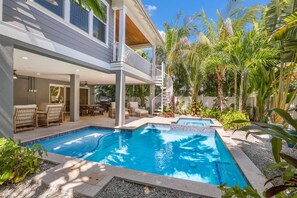 Ein modernes Haus mit Pool, Gartenmöbeln und tropischen Pflanzen.