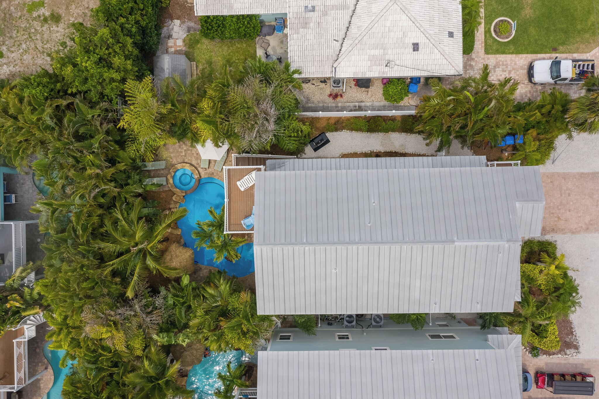 An aerial view of a residential property with a swimming pool, multiple vehicles, and lush greenery.