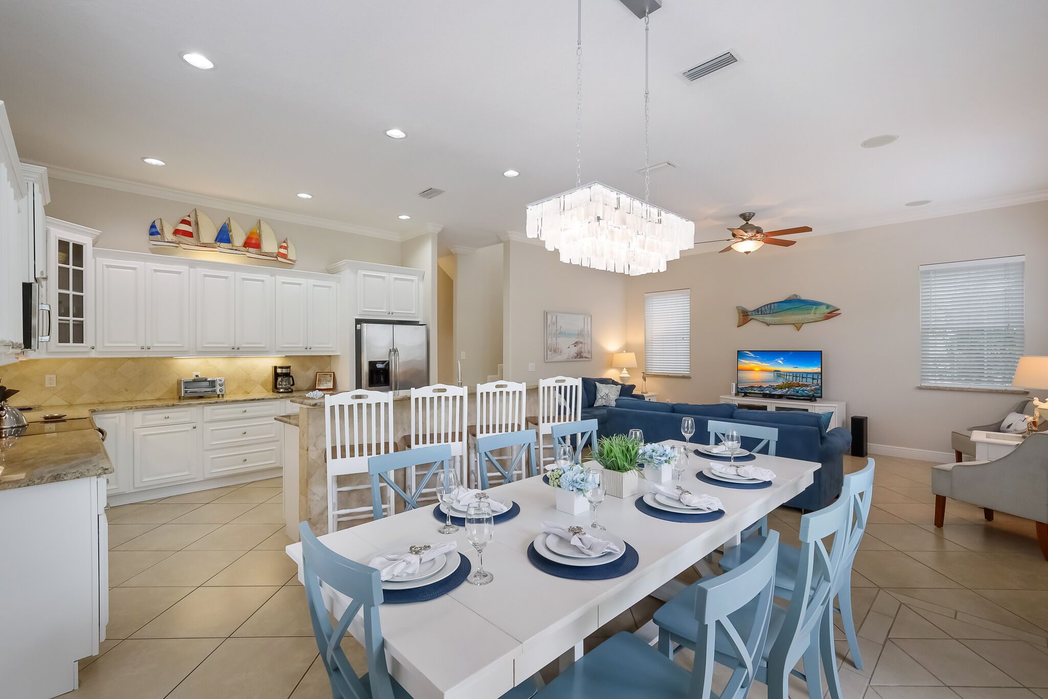 A modern kitchen with white cabinets, a dining area with blue chairs, and a ceiling fan.