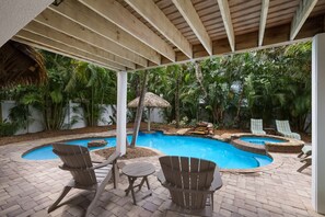 Area piscina con due poltrone Adirondack, un tavolo e una struttura con tetto di paglia.