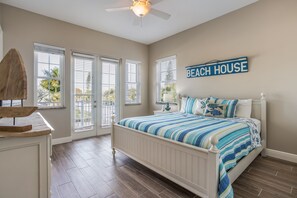 Une chambre avec un lit, un ventilateur de plafond, une pancarte indiquant « MAISON DE PLAGE », et une vue à travers la porte.