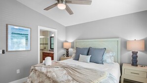 A bedroom with a bed, two bedside lamps, a ceiling fan, a framed picture, a mirror, and a nightstand.