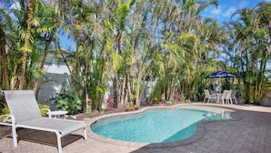 A swimming pool with lounge chairs and a table, surrounded by palm trees and plants.