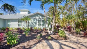 A house with a light blue exterior, a covered porch, and a well-maintained garden with various plants and palm trees.