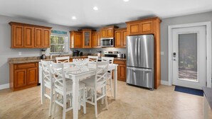 A modern kitchen with wooden cabinets, stainless steel appliances, and a white dining table.