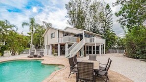 A two-story house with a pool, outdoor seating, and a staircase leading to the upper level. - Hammock Dreams - Canal Home with Pool and Dock Near Beach (Anna Maria)