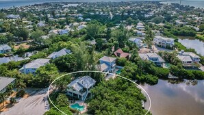 An aerial view of a residential area with houses, a large body of water, and a highlighted house with a swimming pool. - Hammock Dreams - Canal Home with Pool and Dock Near Beach (Anna Maria)
