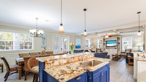 A spacious kitchen with a large island, blue cabinets, and a dining area with wicker furniture. - Poseidons Palace! Family Fun and Gulf Views! (Holmes Beach)