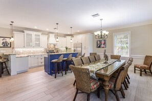 Uma cozinha espaçosa com uma ilha central, banquetas, uma mesa de jantar com cadeiras e iluminação pendente.
