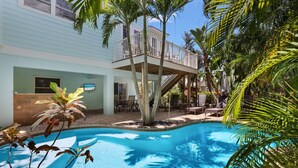 A pool area with a covered deck, lounge chairs, and a staircase leading to an upper level.