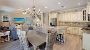 A spacious kitchen with a central island, a dining area with wicker chairs, and a large chandelier.