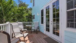 A covered outdoor deck with wicker chairs and a small table, surrounded by lush greenery.