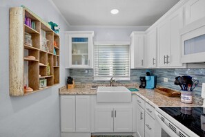 A kitchen with white cabinets, a granite countertop, a sink, and a window with blinds.