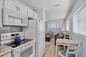 A compact kitchen with a stove, microwave, and refrigerator. There is a dining area with a table and chairs, and a sofa.