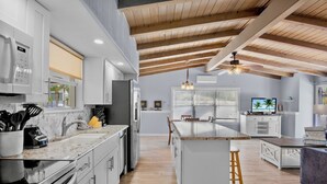 A modern kitchen with white cabinetry, a central island, and a wooden ceiling.