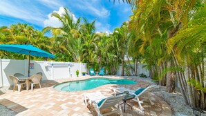 A backyard with a swimming pool, lounge chairs, and a table with chairs.