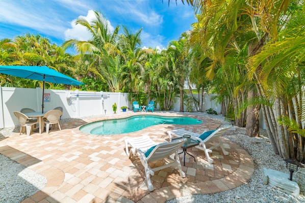 A backyard with a swimming pool, lounge chairs, and a table with chairs. - Home with Private Backyard and Heated Pool - Gulf Breeze Villa B (Holmes Beach)