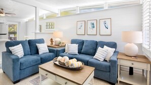 A modern living room with a blue sofa set, a coffee table with towels, and framed artwork on the wall.