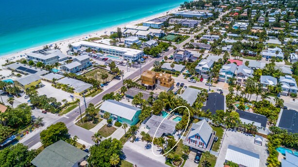 An aerial view of a coastal town with a beach, residential buildings, and a highlighted property with a swimming pool.