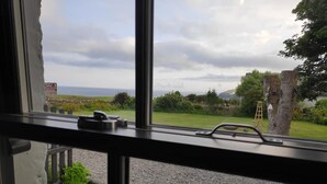 A view through a window with a gravel ground, a wooden ladder, and a grassy area with trees. - Bespoke 1 Bed Cottage in Dunbeath Village (Dunbeath)