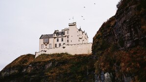 A castle-like building with multiple towers and a fortified wall, situated on a rocky hill. - Bespoke 1 Bed Cottage in Dunbeath Village (Dunbeath)