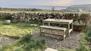 A garden with a wooden bench and table, surrounded by a stone wall and a view of the sea. - Bespoke Hand Built Shepherds Hut in Dunbeath (Dunbeath)
