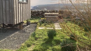 A wooden cabin with a stone wall and garden. - Bespoke Hand Built Shepherds Hut in Dunbeath (Dunbeath)