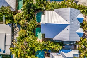 Vista aérea de un resort con varias piscinas, abundante vegetación y un edificio principal con un diseño de techo distintivo.