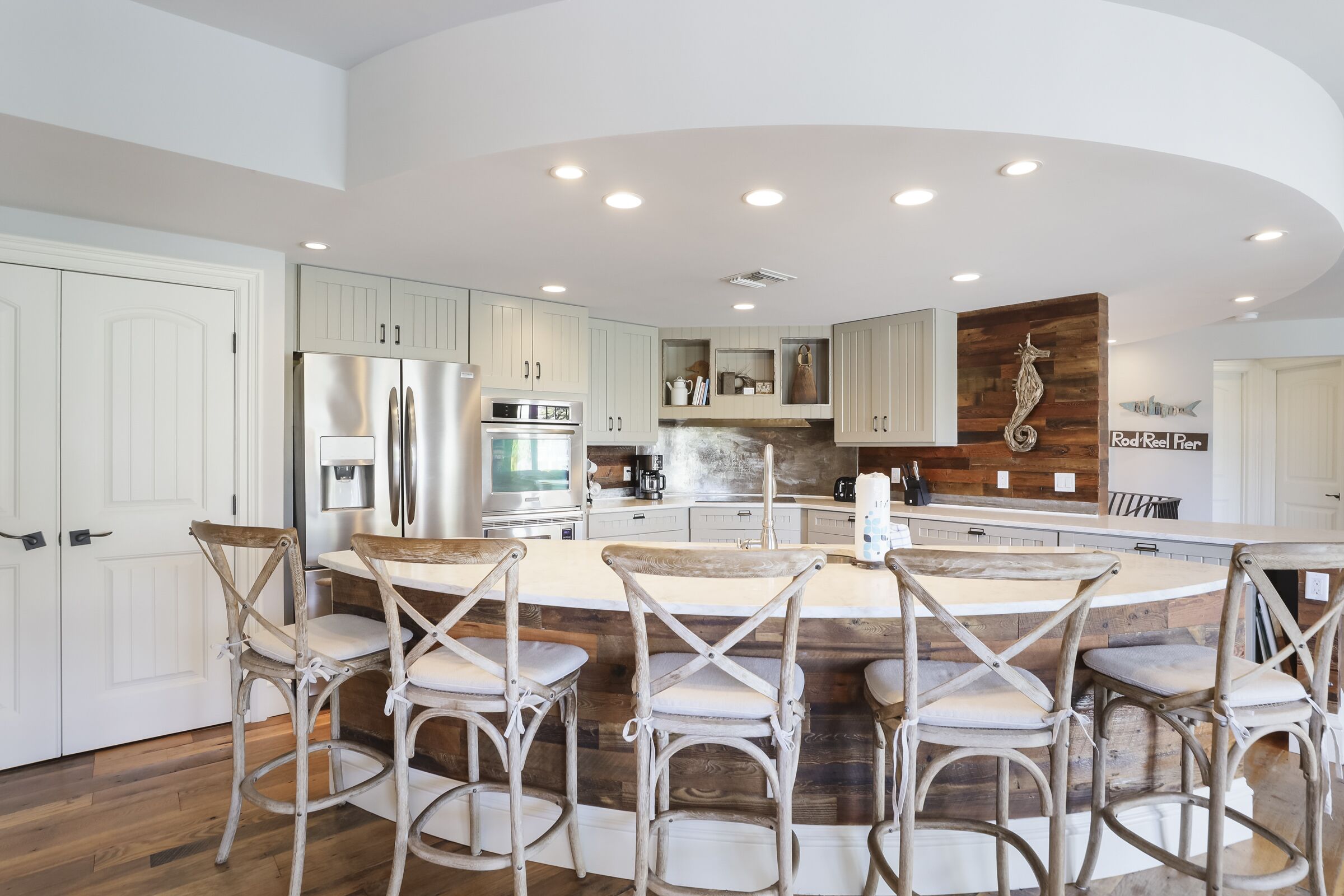 A modern kitchen with a central island, bar stools, and a wooden accent wall.