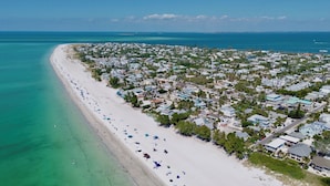 Luchtbeeld van een kustplaatsje met een lang zandstrand, bezaaid met parasols en mensen.