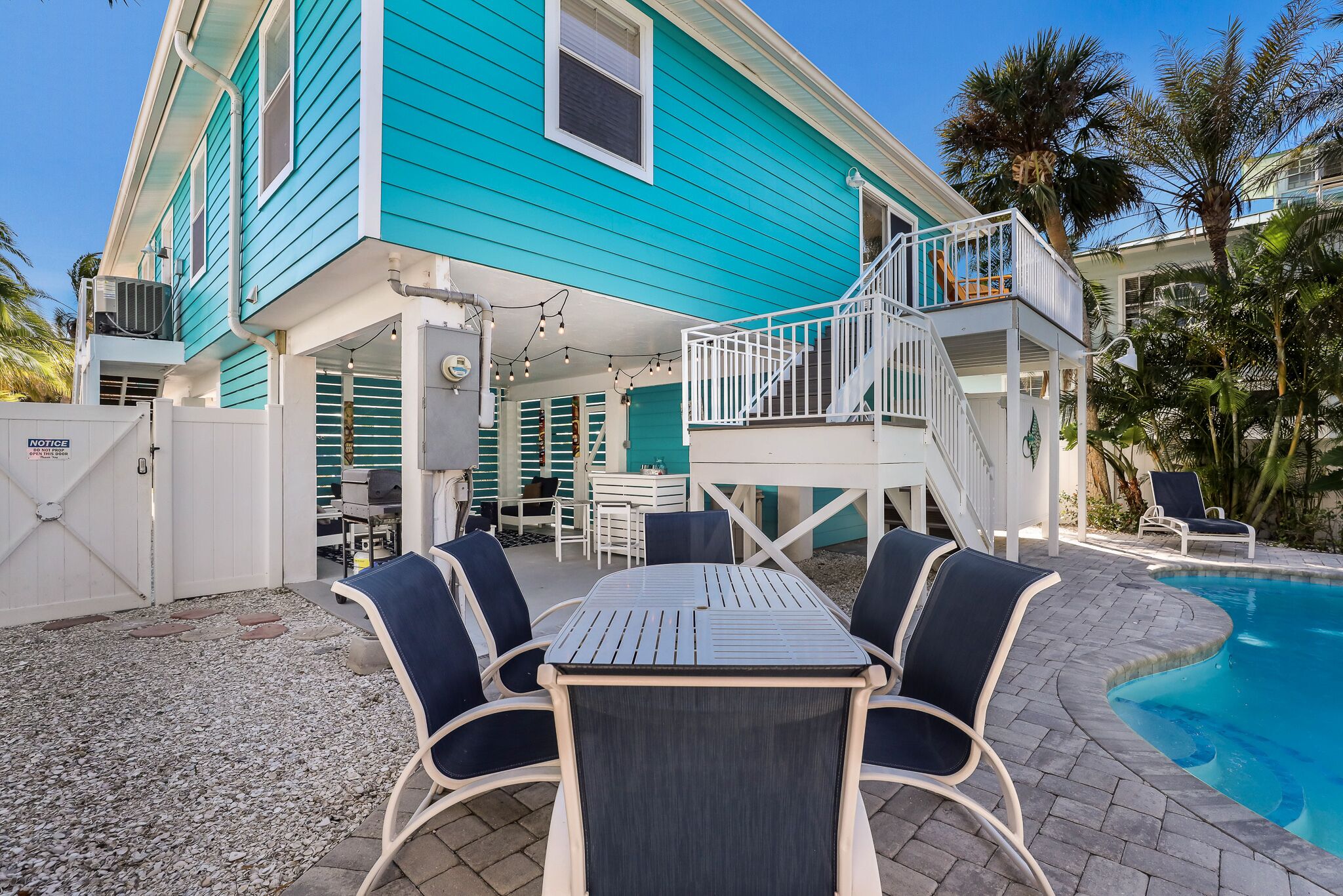 A turquoise house with a pool, outdoor seating, and a covered patio area.
