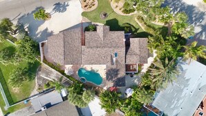 Une vue aérienne d’une maison avec une piscine, entourée de palmiers et d’une pelouse bien entretenue.
