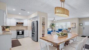 Una cocina moderna con armarios blancos, electrodomésticos de acero inoxidable y una mesa de comedor de madera con sillas blancas.