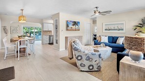 Amplia sala de estar con un sofá azul, un sillón estampado y una zona de comedor con mesa de madera y sillas blancas.