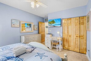 A bedroom with a bed, dresser, desk, chair, wardrobe, ceiling fan, and artwork on the walls. - Beachfront Rental with Ocean Views, Close to Restaurants and Shopping! (Bradenton Beach)