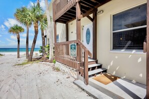 A beachfront property with a wooden staircase leading to a covered porch, a sign indicating a beach pad, and a view of the ocean.