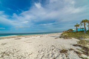 A beach with white sand, ocean waves, and palm trees.