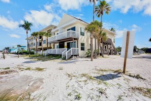 A beachfront hotel with multiple balconies, a sandy beach in front, and palm trees.