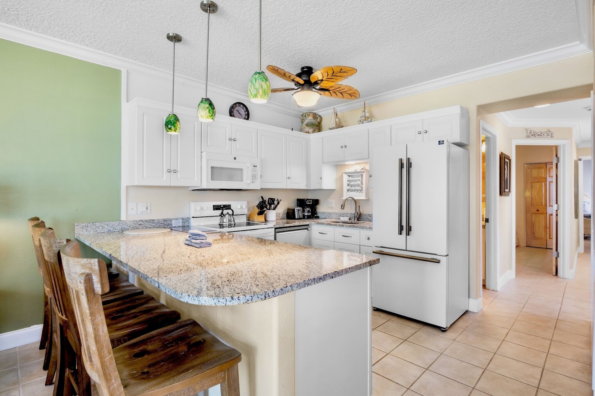A kitchen with white cabinets, a granite countertop, a built-in oven, a refrigerator, and a ceiling fan.