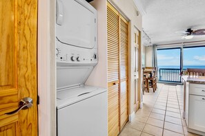 A laundry room with a washing machine and dryer, a wooden door, and a view of a balcony with a table and chairs. - Beachfront Rental with Ocean Views, Close to Restaurants and Shopping! (Bradenton Beach)