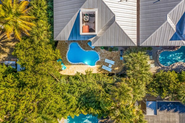 An aerial view of a resort with multiple swimming pools surrounded by lush greenery and palm trees. - Beautiful Guest House Near the Beach with Private Pool! (Anna Maria)