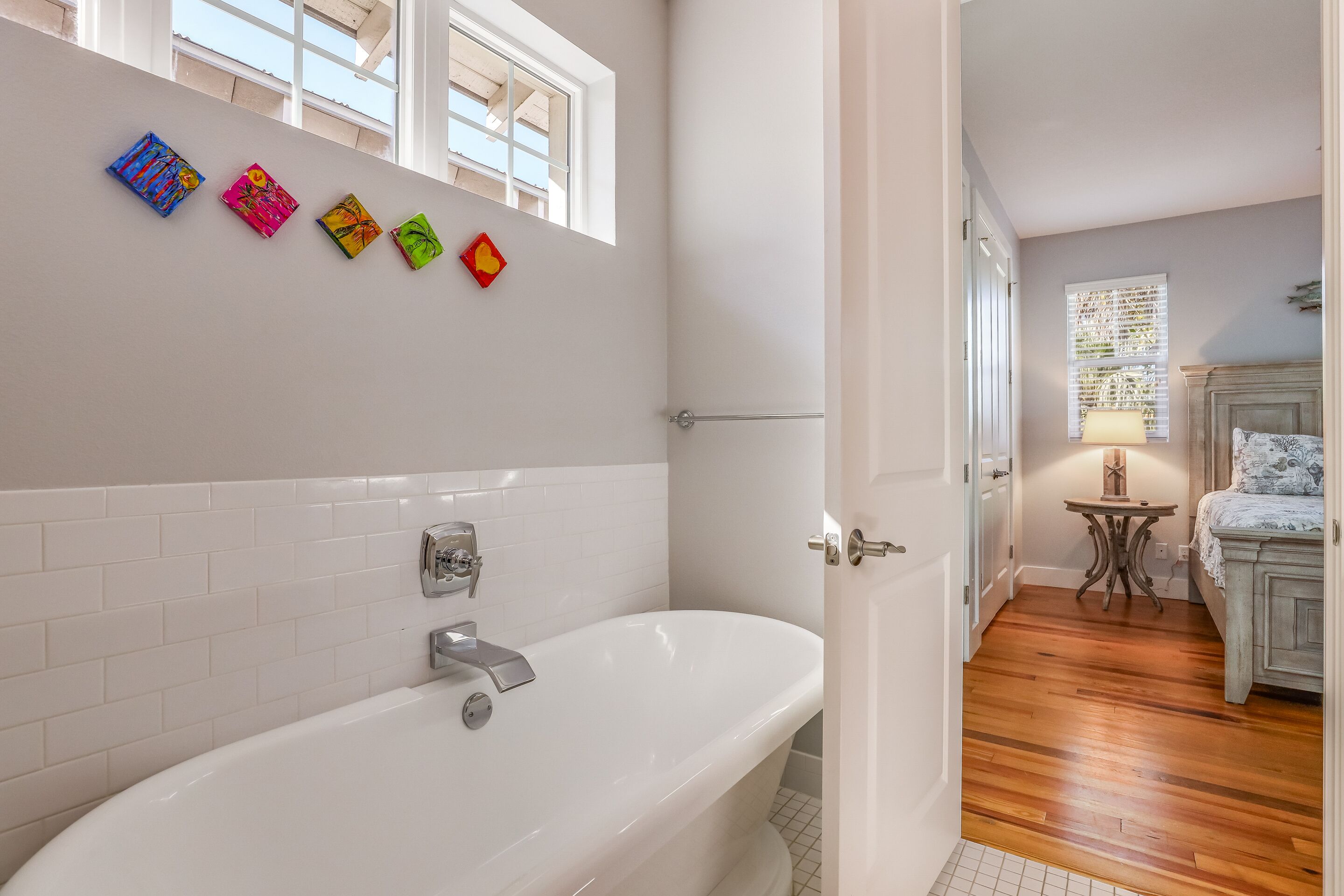 Un baño moderno con una bañera independiente, paredes de azulejos blancos y una ventana con persianas.
