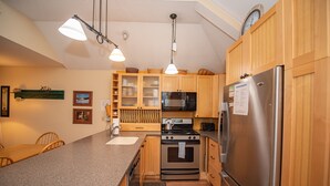 Eine Küche mit Holzausstattung, einem Edelstahlkühlschrank, einer Mikrowelle, einem Backofen und einer Arbeitsplatte aus Granit.